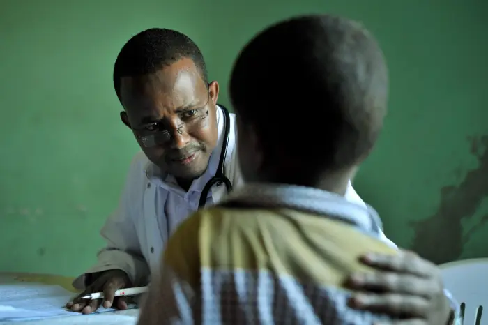 Male African doctor Talking To a Young Boy in Local Clinic